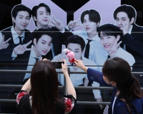 BTS fans take photos of BTS merchandise with a BTS banner displayed on the HYBE building in the background