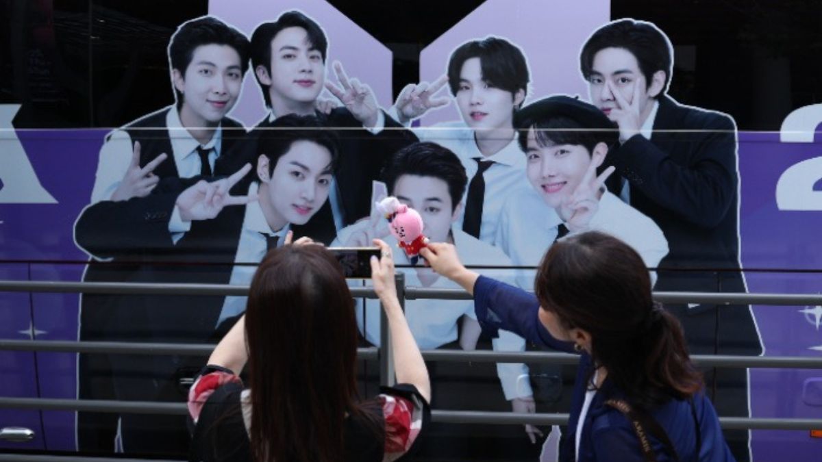BTS fans take photos of BTS merchandise with a BTS banner displayed on the HYBE building in the background