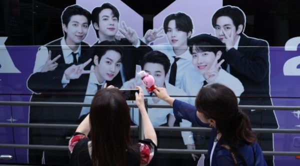BTS fans take photos of BTS merchandise with a BTS banner displayed on the HYBE building in the background
